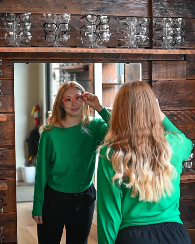 A young woman looking in the mirror and trying on eyeglass frames